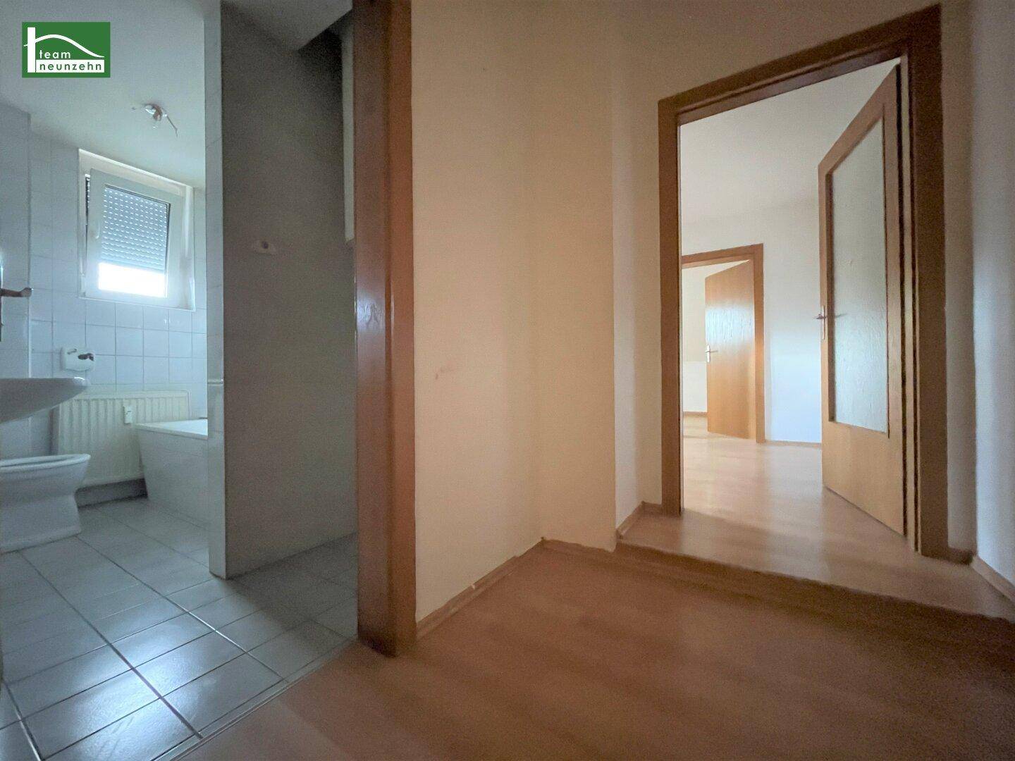 Blick von einem Raum in ein gefliestes Badezimmer und einen weiteren Raum mit Laminatboden.