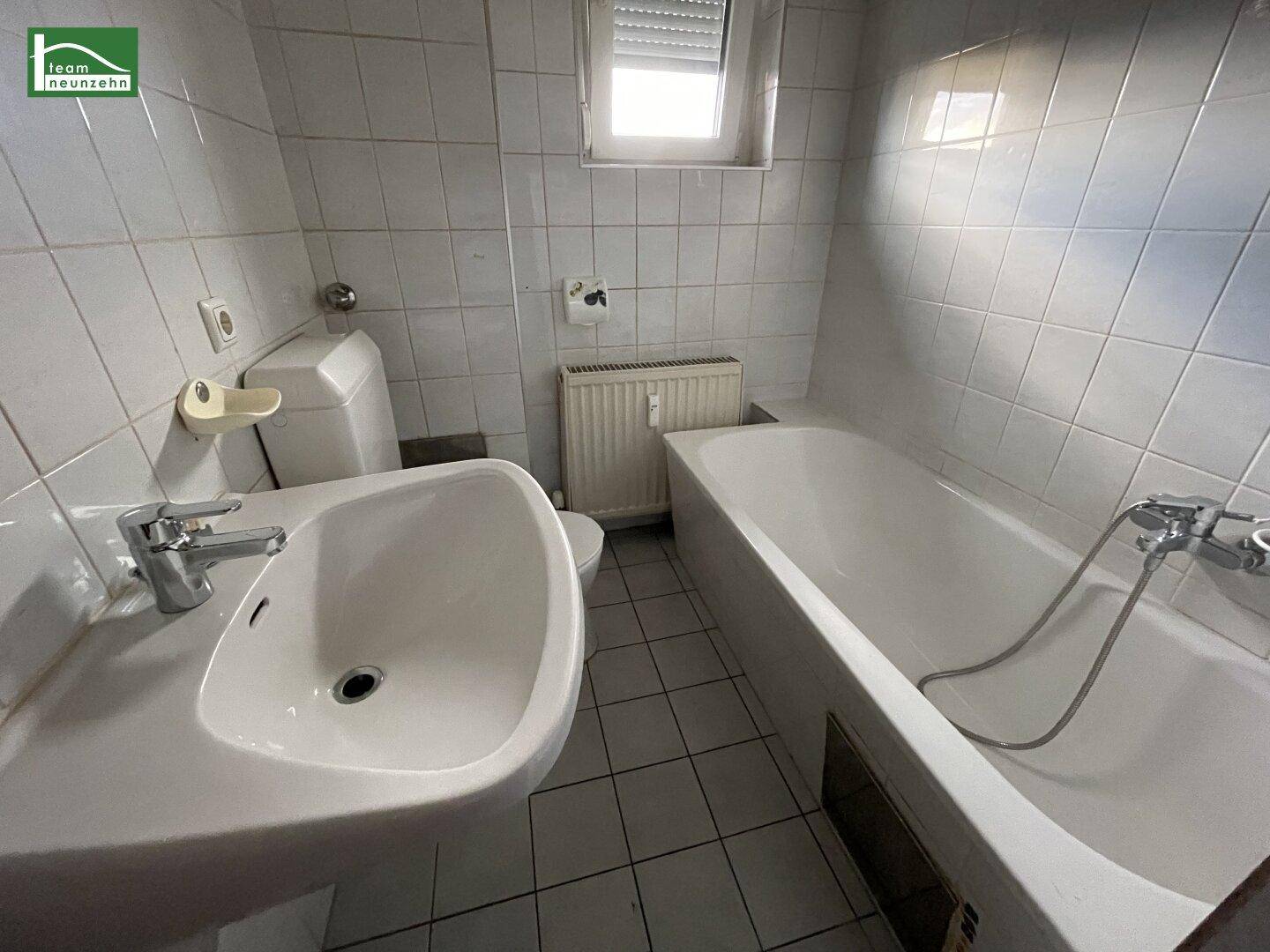 Gefliestes Badezimmer mit Badewanne, Waschbecken, Toilette und einem Fenster für Tageslicht.