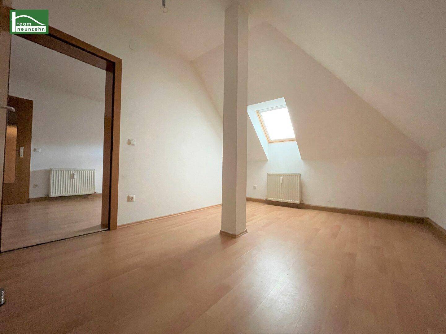 Dachgeschossraum mit Laminatboden, Dachschräge und einem Dachfenster, das Tageslicht hereinlässt.