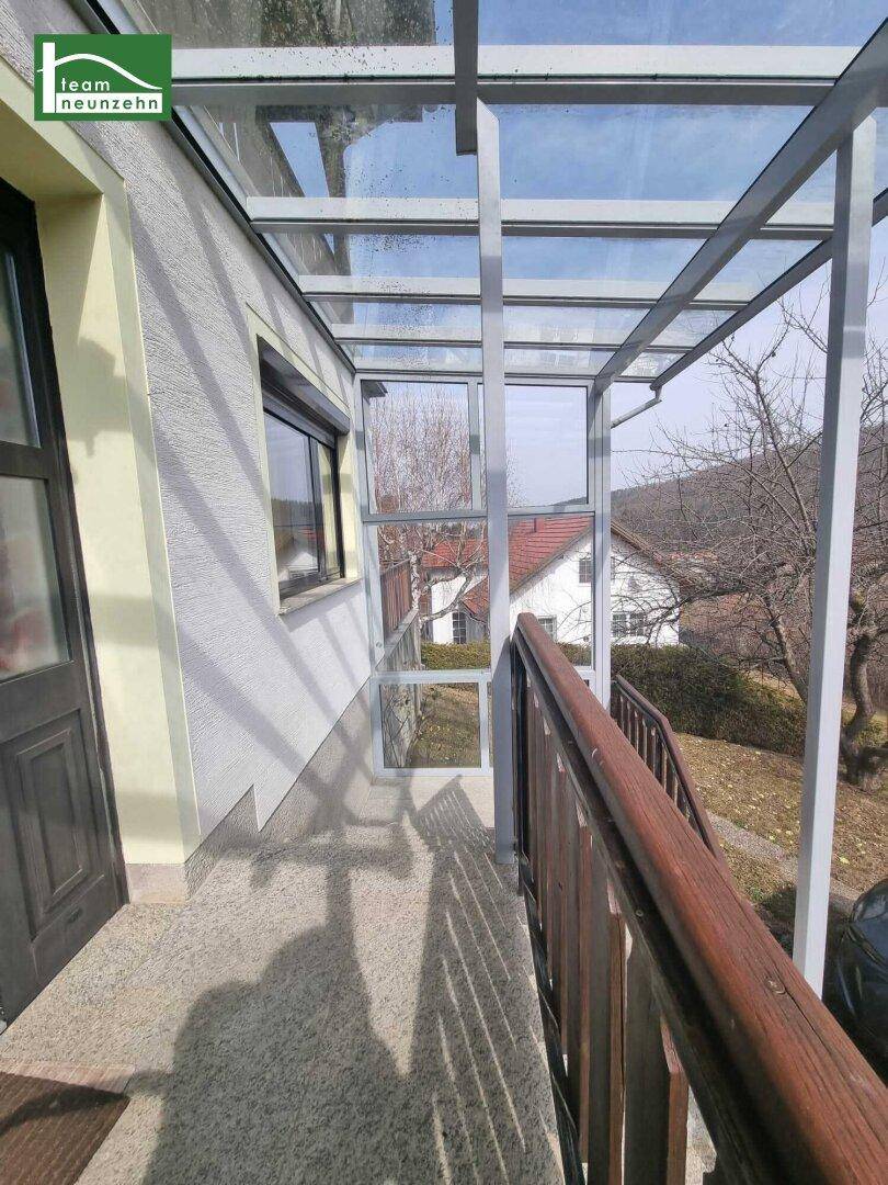 Überdachter Balkon mit Glasdach und Holzgeländer, bietet einen Blick auf die Umgebung.