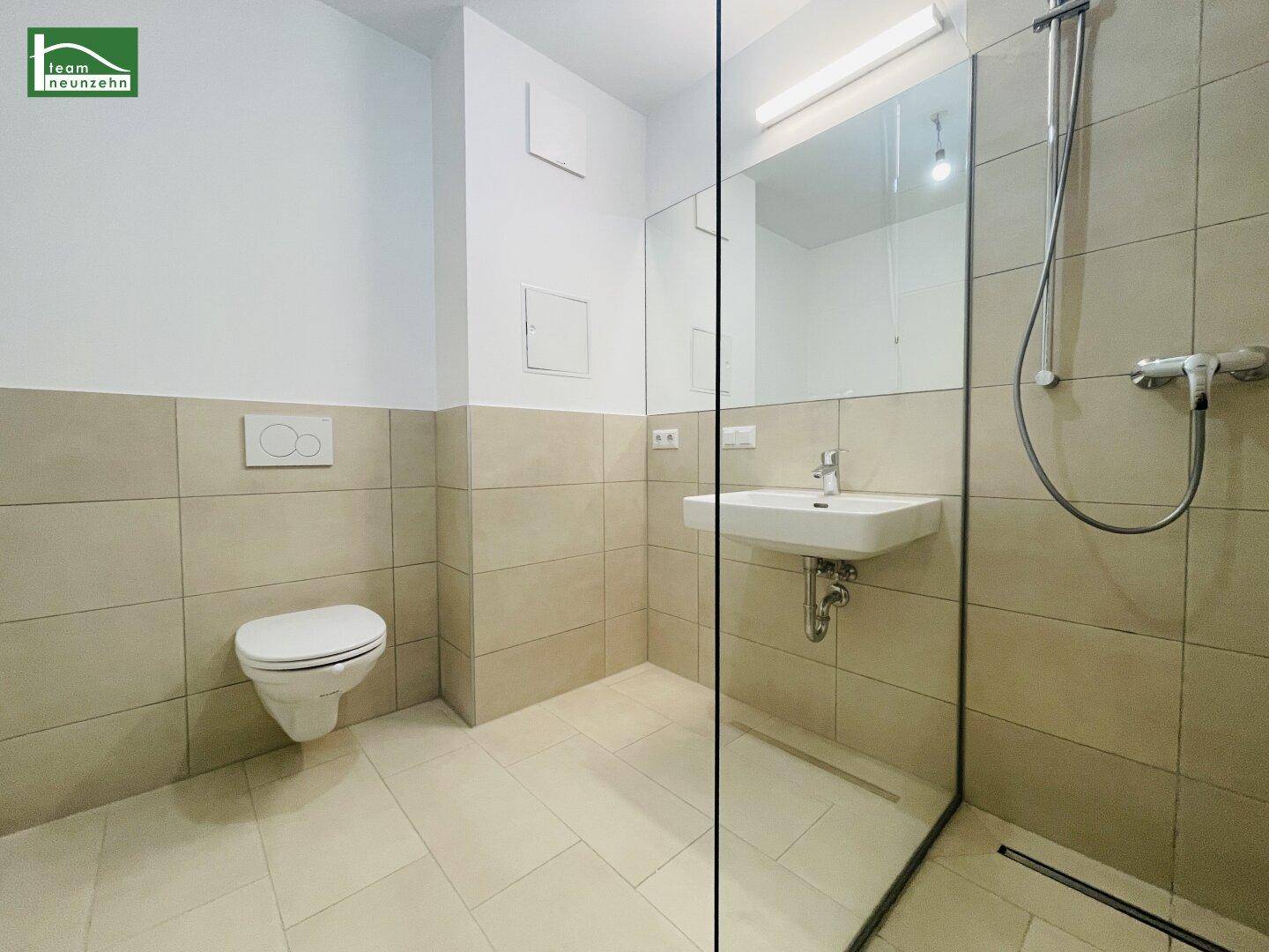 Modernes Badezimmer mit beigefarbenen Fliesen, wandhängendem WC und ebenerdiger Dusche.
