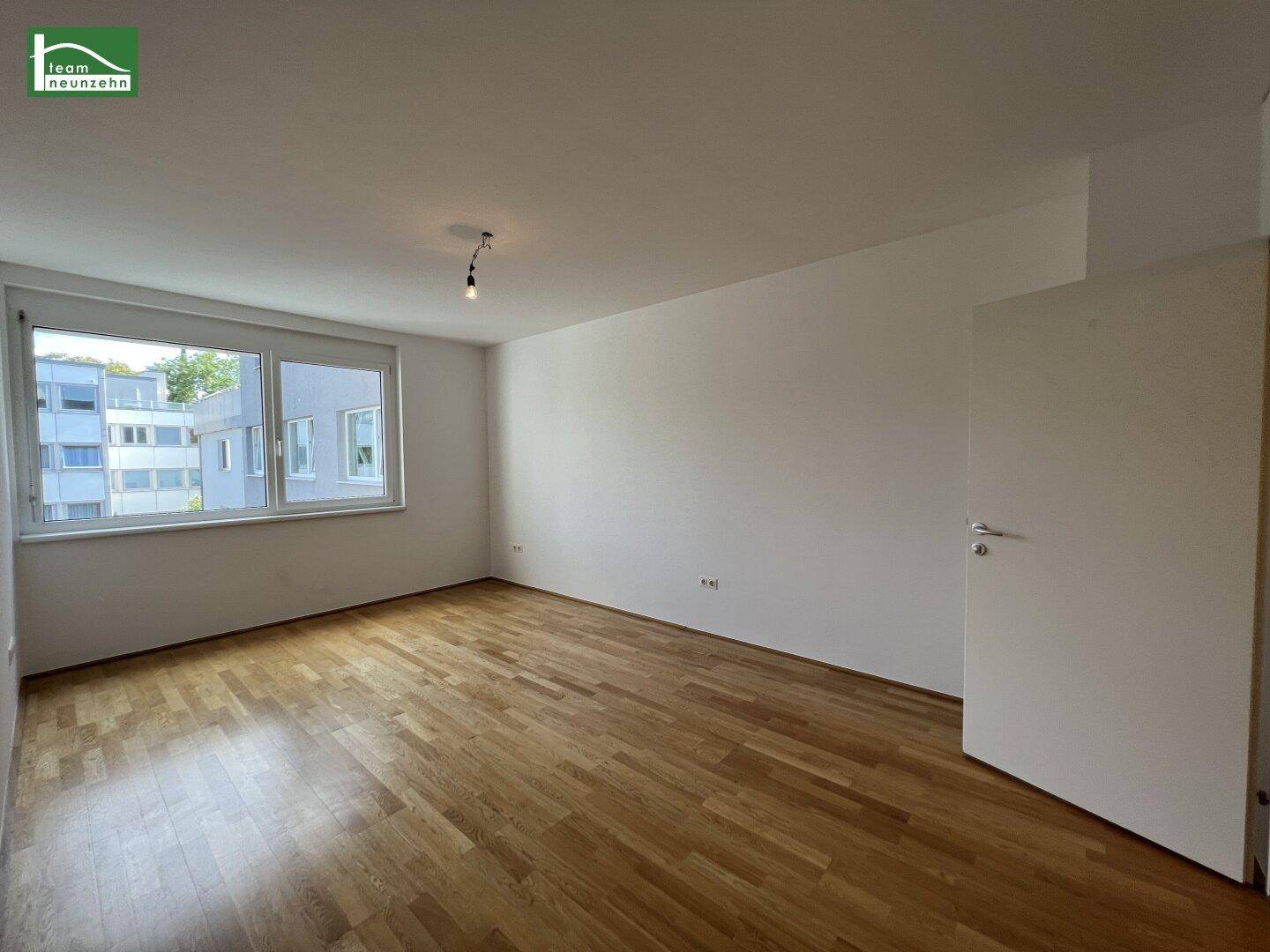 Helles Schlafzimmer mit Parkettboden und Blick auf die umliegenden Gebäude.