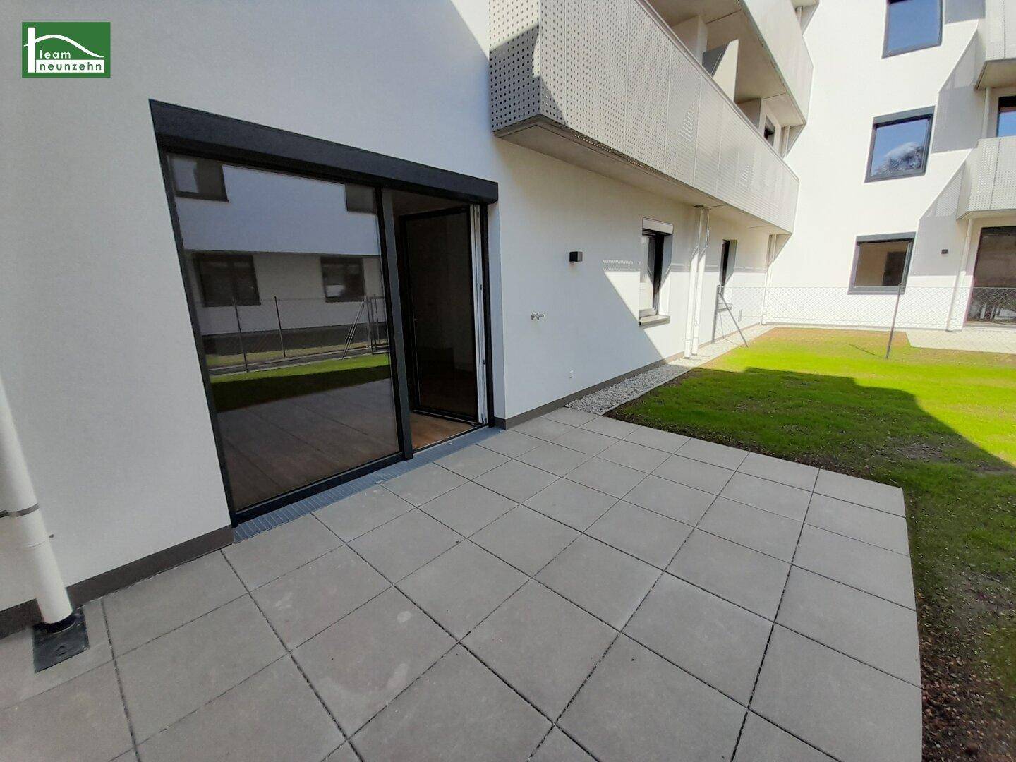 Sonnige Terrasse mit direktem Zugang zum Garten und Blick auf die moderne Fassade.