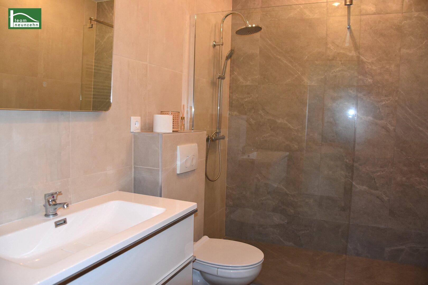Modernes Badezimmer mit beigefarbenen Fliesen, Waschtisch und einer geräumigen begehbaren Dusche.