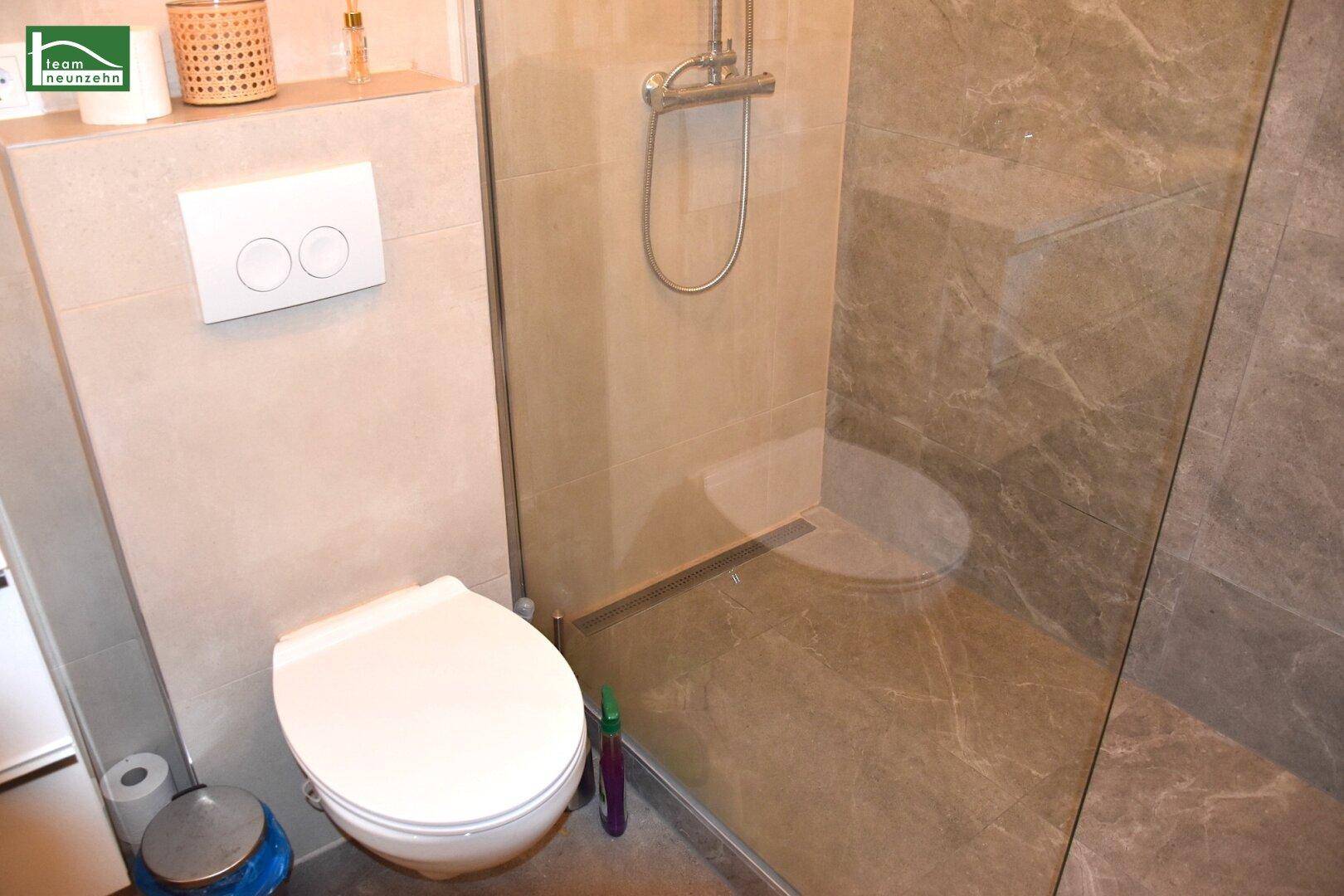 Detaillierte Ansicht des WCs und der modernen, ebenerdigen Dusche mit Glasabtrennung.