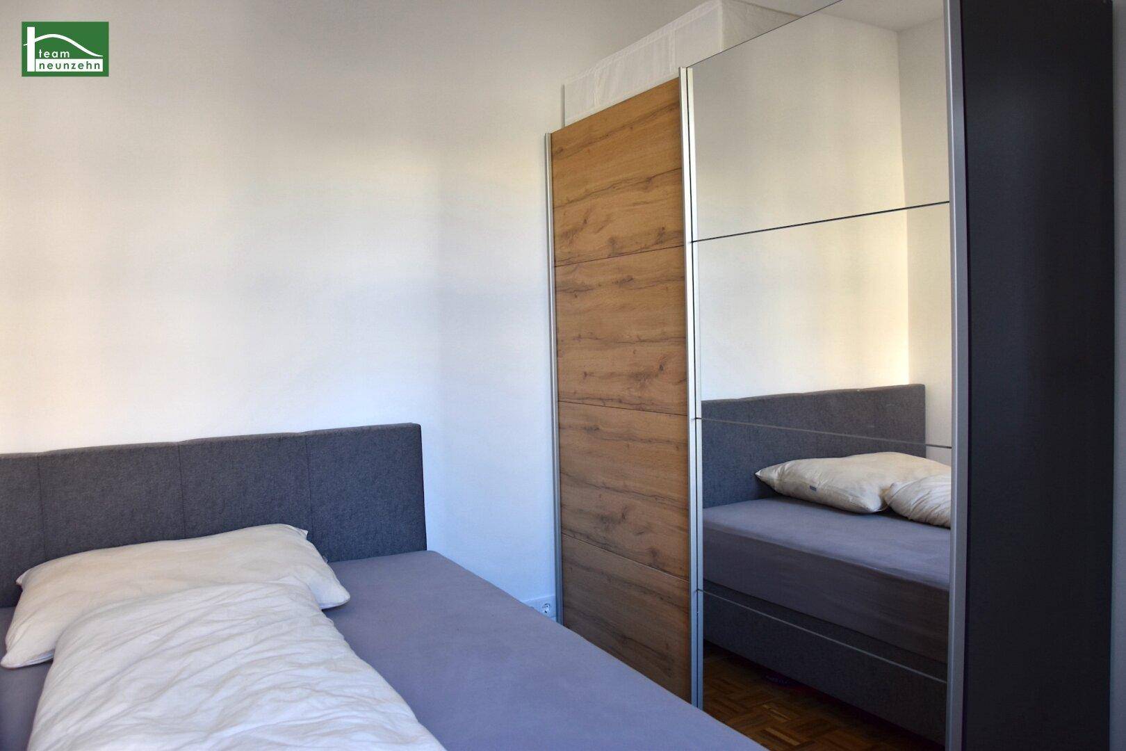 Schlafzimmer mit Bett und modernem Kleiderschrank mit Spiegel- und Holzfronten, funktional eingerichtet.