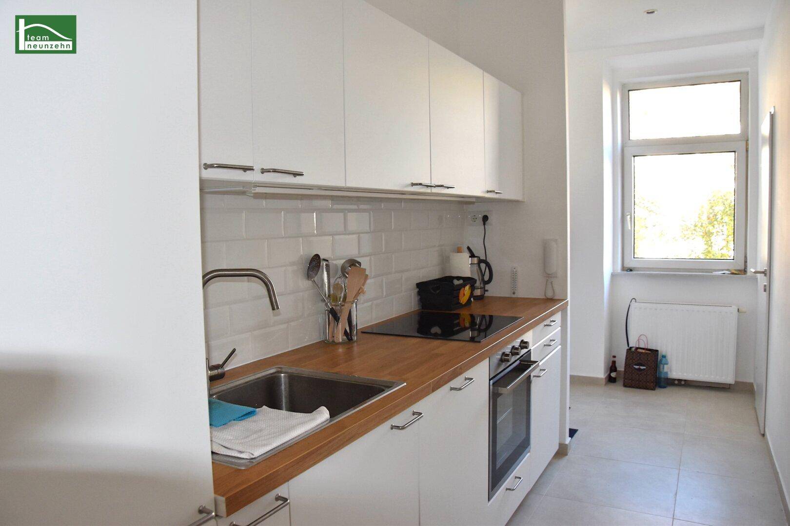 Moderne Küche mit weißen Schränken, Holz-Arbeitsplatte und integrierten Geräten, hell und funktional.