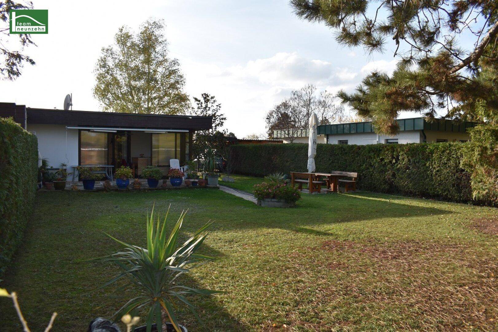Weitläufiger Garten mit großer Rasenfläche, Hecken und einer Terrasse am hinteren Teil des Hauses.