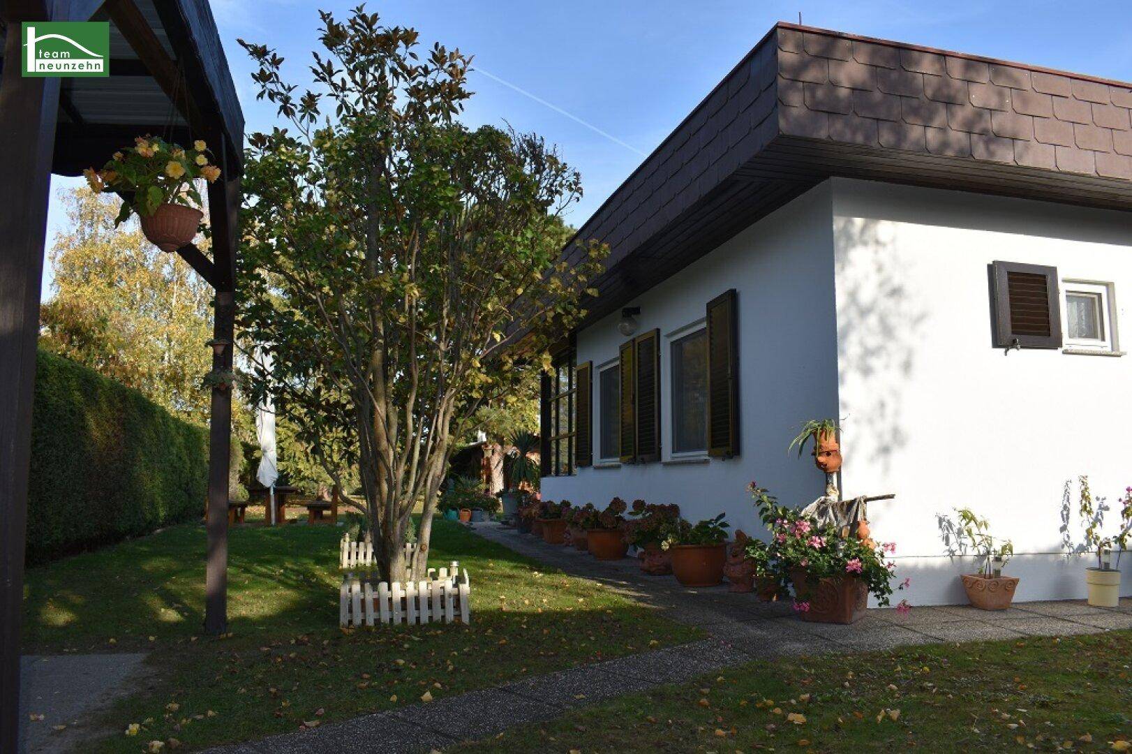 Seitenansicht des Hauses mit Fensterläden, einem gepflasterten Weg und blühenden Pflanzen im Vorgarten.