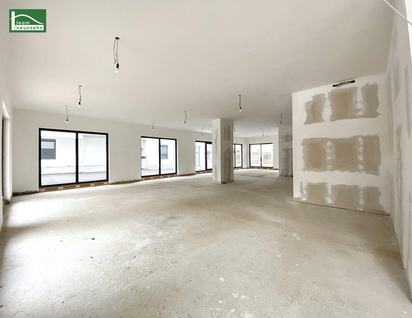 Heller Gewerberaum im Rohbau mit großen Fensterfronten und Säulen, bereit für den Ausbau.