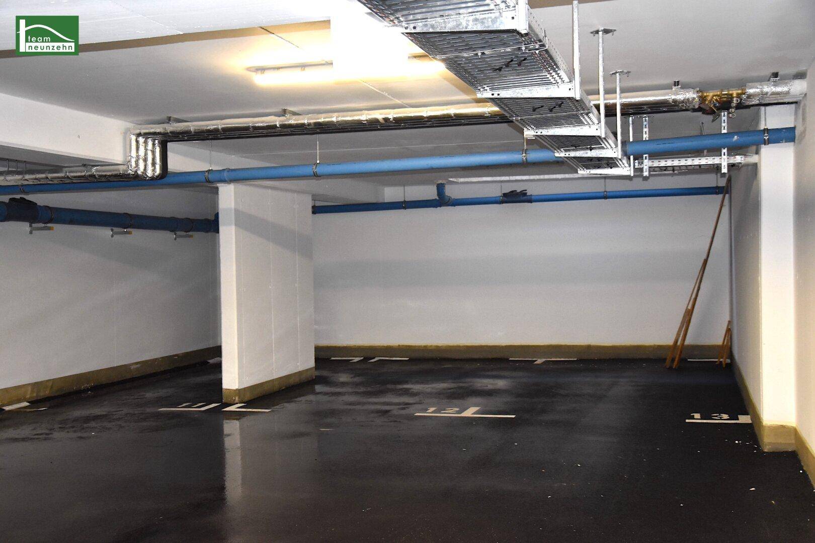 Leere Tiefgarage mit sichtbaren Versorgungsleitungen und Kabeltrassen an der Decke.