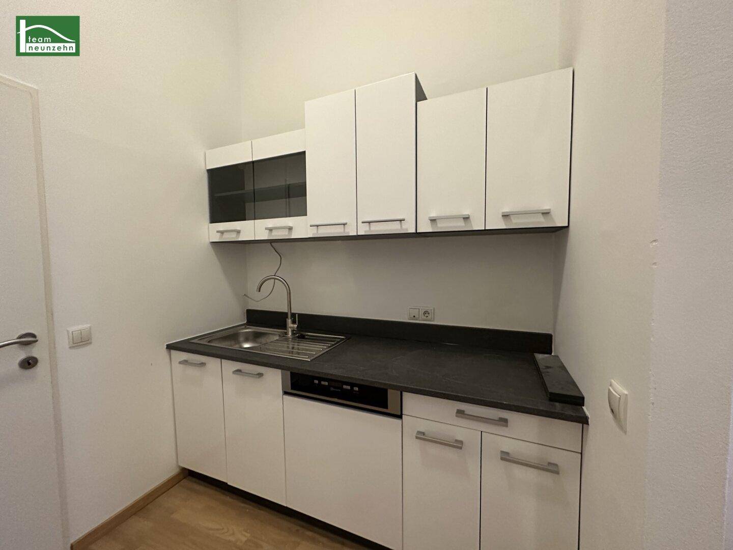Kompakte Einbauküche mit weißen Schränken, Spüle und integriertem Geschirrspüler für effizientes Kochen.