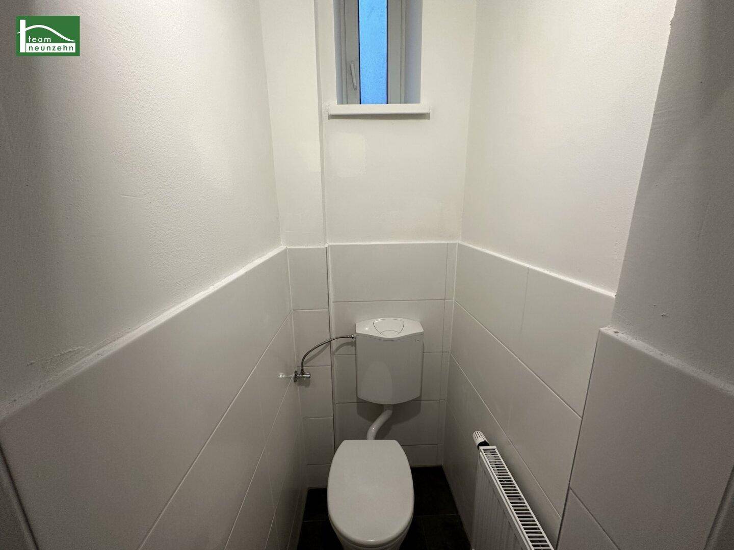 Separates WC mit Fenster, weiß gefliesten Wänden und Heizkörper für zusätzlichen Komfort.