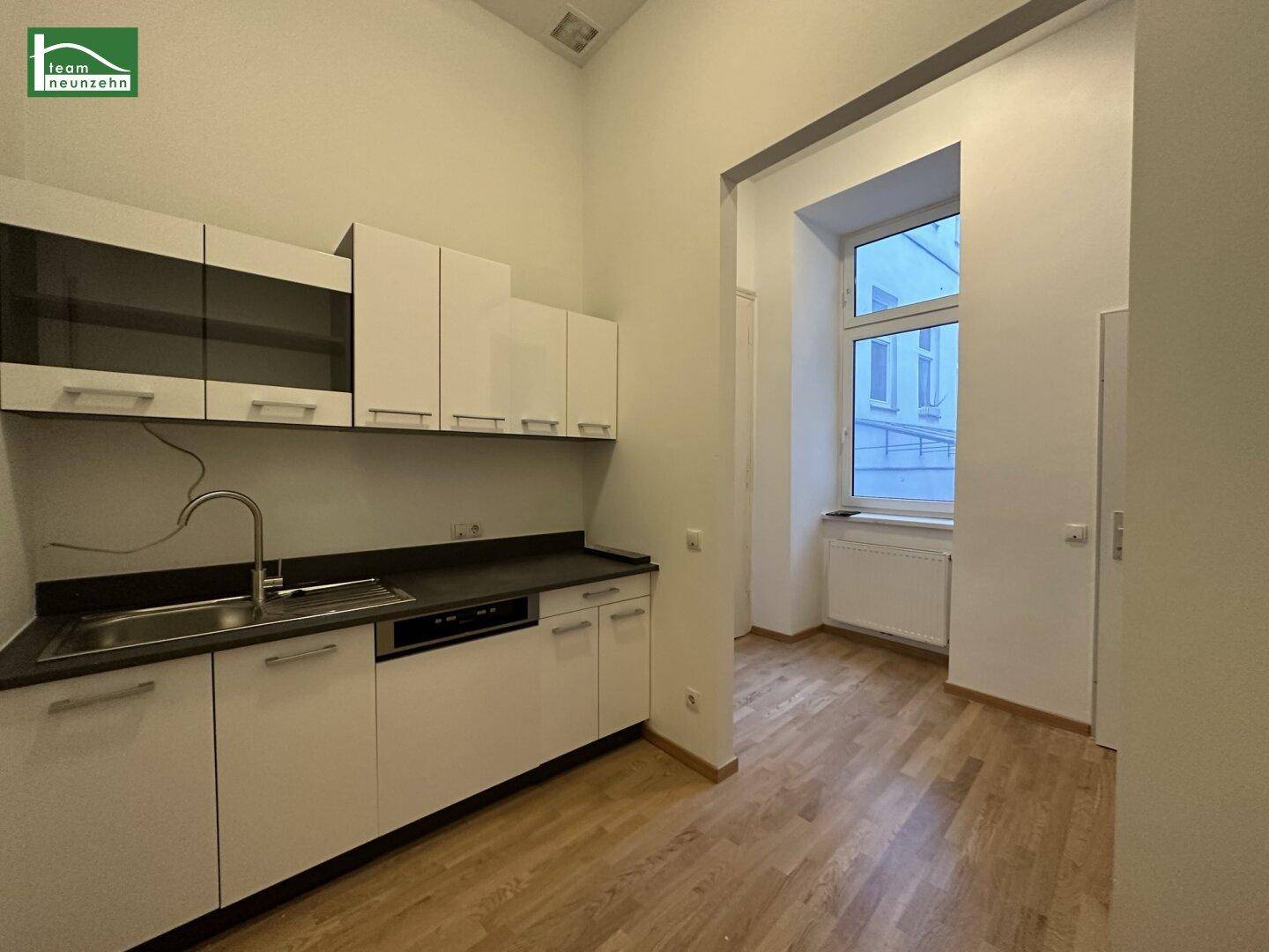 Funktionale Küchenzeile mit weißen Schränken, dunkler Arbeitsplatte und Fenster mit Tageslicht.