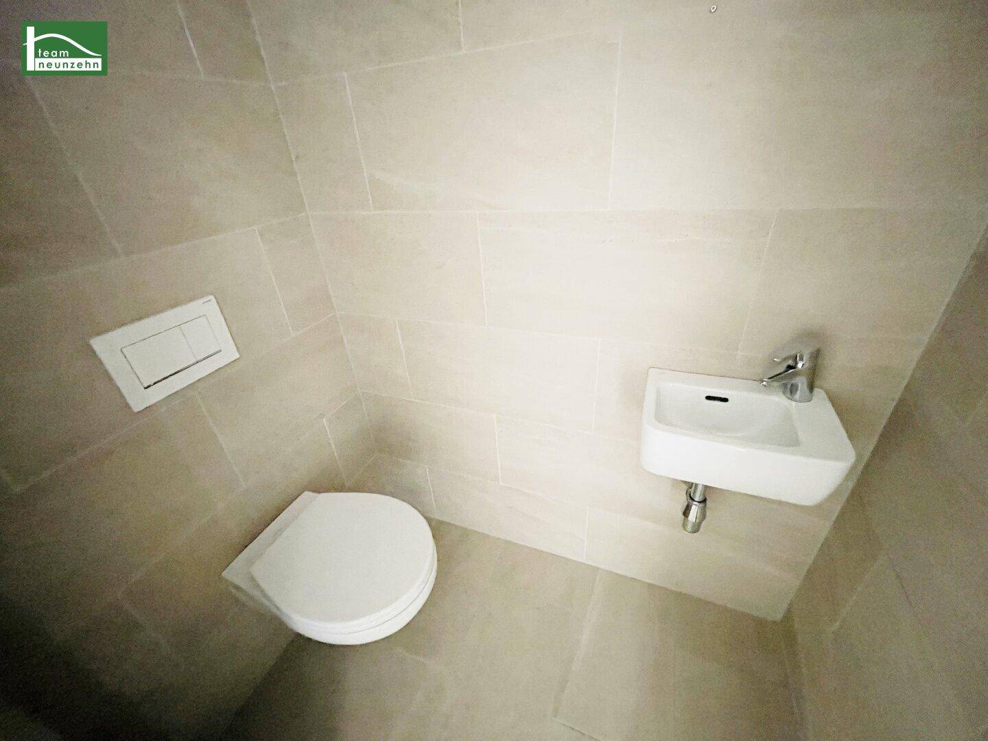 Modernes Gäste-WC mit wandhängender Toilette, kleinem Waschbecken und hellen Fliesen.