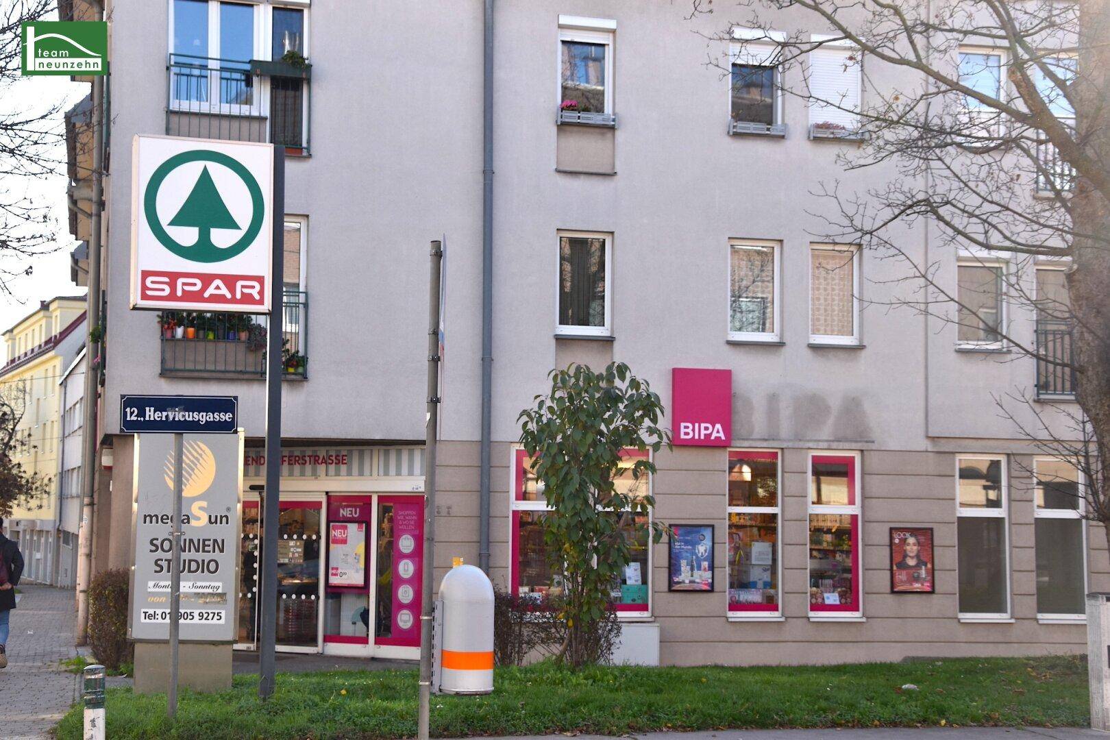 Gebäudeansicht mit Geschäften wie SPAR und BIPA, die die Nahversorgung in der Umgebung zeigen.