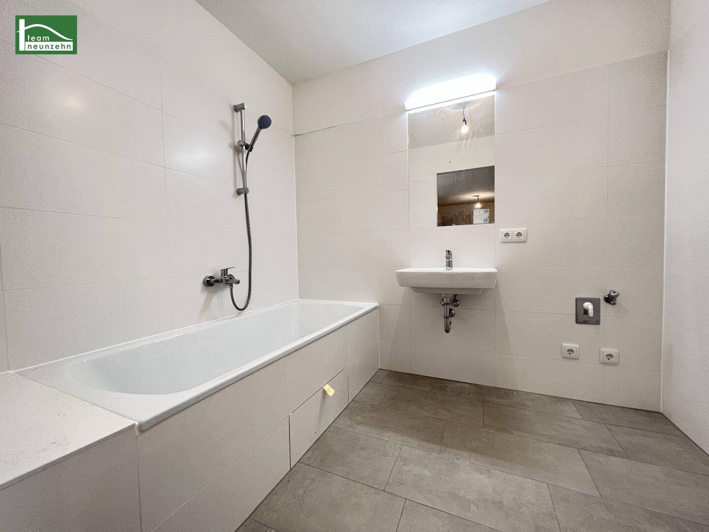Helles Badezimmer mit weißen Fliesen, Badewanne, Waschbecken und großem Spiegel.