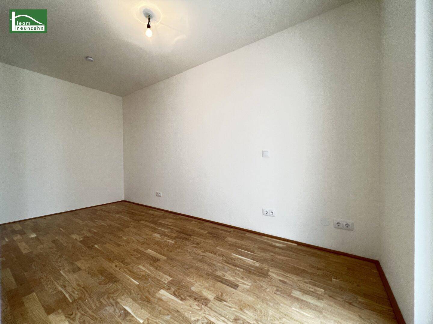 Heller, leerer Raum mit Holzboden und weißen Wänden, vielseitig nutzbar für Wohnzwecke.