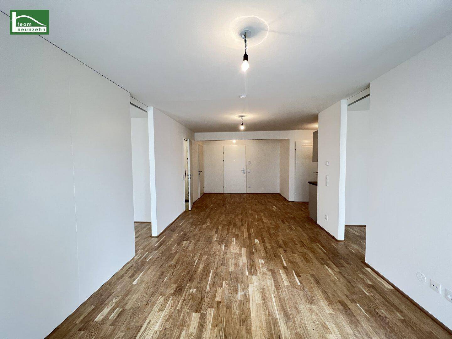 Leerer, heller Wohnbereich mit Holzboden und weißen Wänden, bereit zur individuellen Gestaltung.