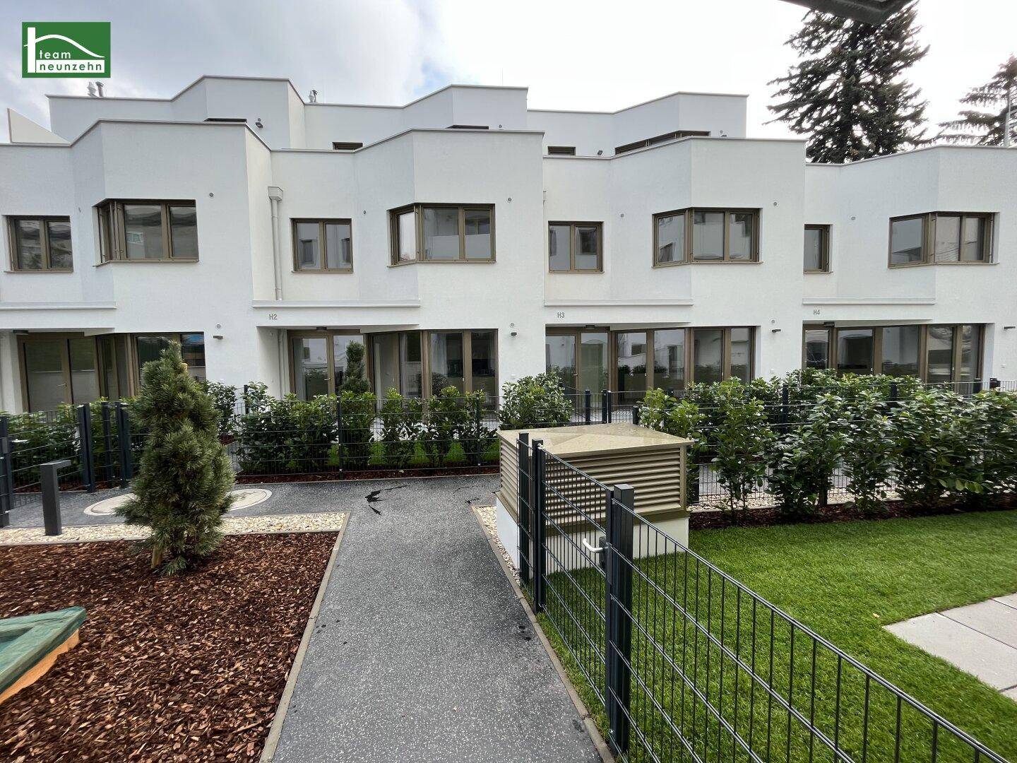 Reihenhäuser mit moderner Architektur, weißer Fassade und gepflegten Vorgärten mit Rasenflächen.