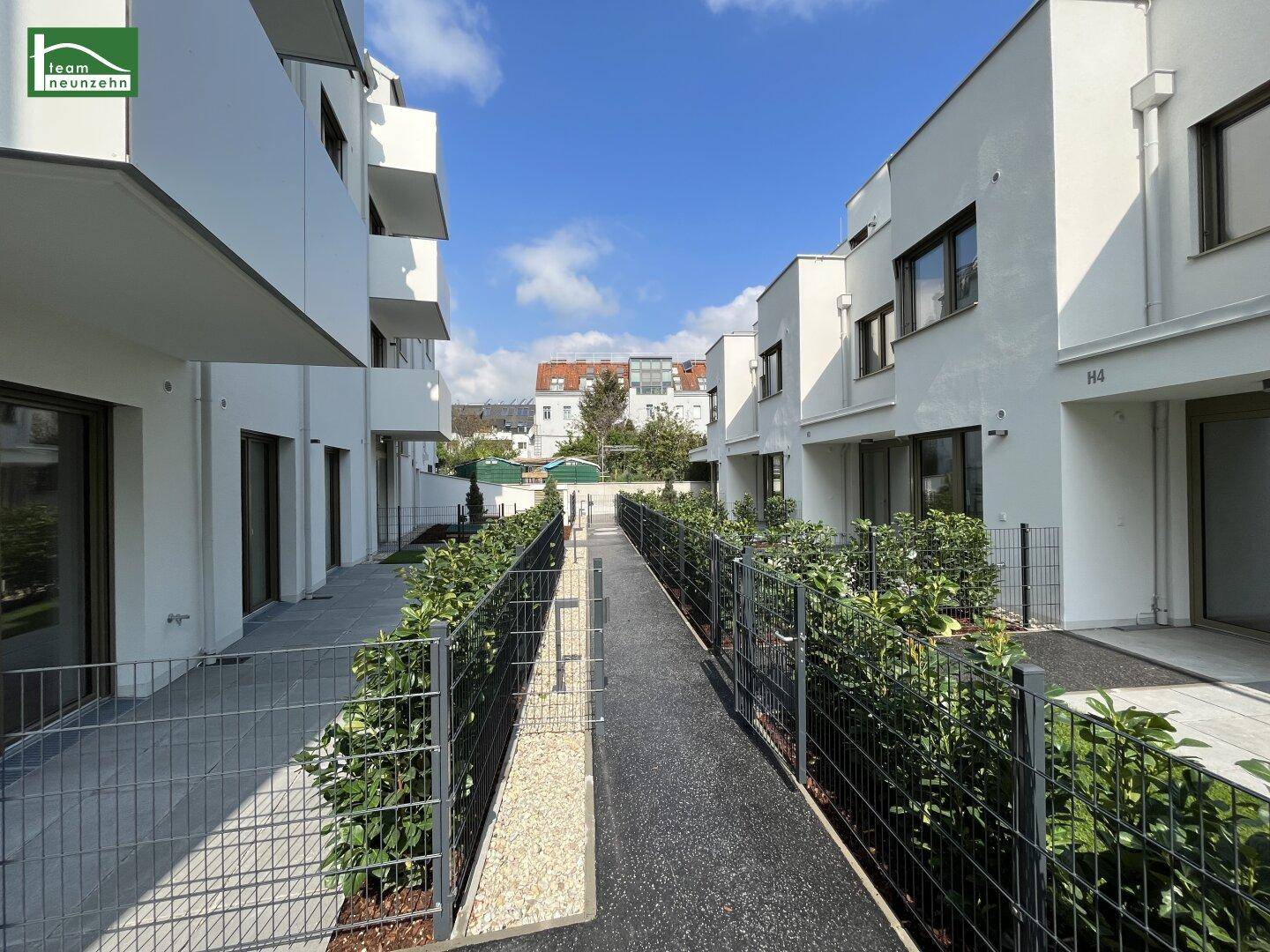 Moderne Wohngebäude mit weißer Fassade, einem gepflasterten Weg und kleinen Grünflächen unter blauem Himmel.