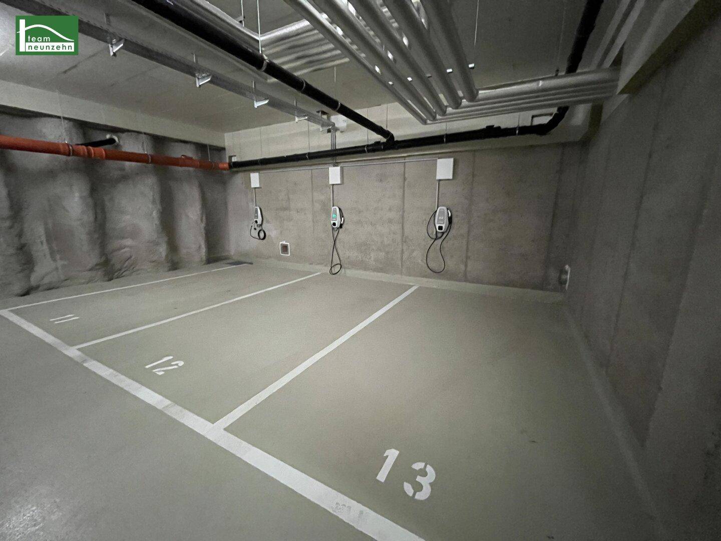 Tiefgarage mit mehreren markierten Stellplätzen und Ladestationen für Elektrofahrzeuge an der Wand.