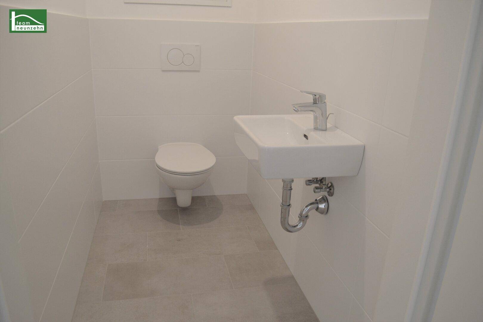 Modernes Gäste-WC mit weißen Fliesen, wandhängendem WC und kleinem Waschbecken.