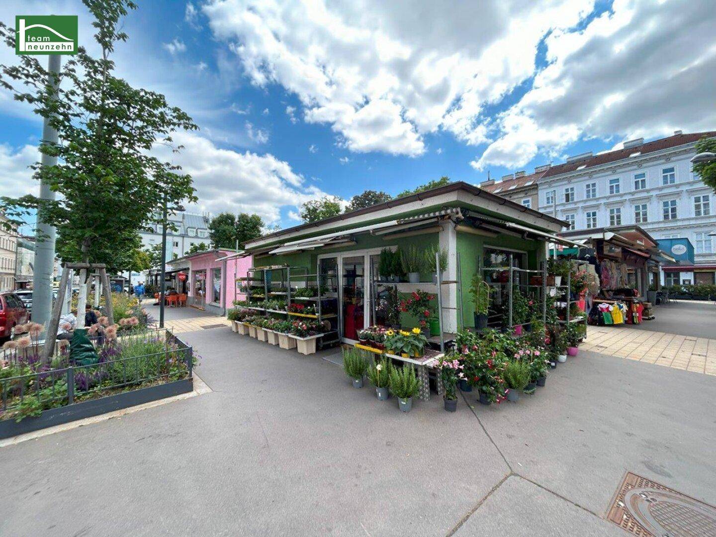 Lebhafter Außenbereich mit einem Blumenladen und weiteren Marktständen unter blauem Himmel.
