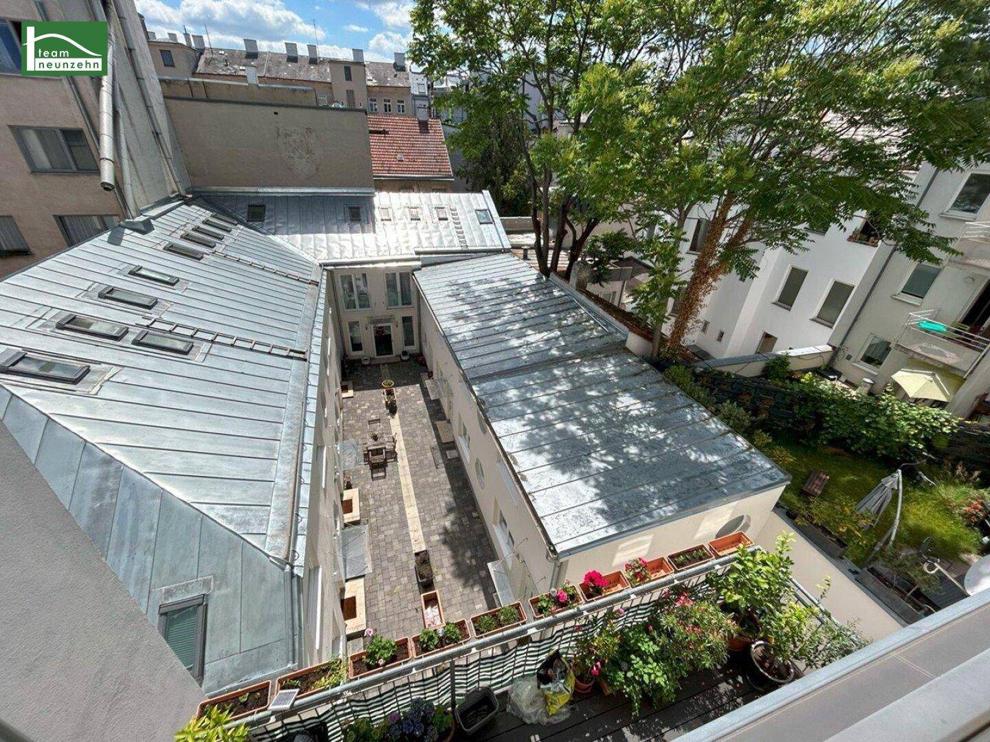 Blick von oben auf einen begrünten Innenhof mit Sitzgelegenheiten und umliegenden Gebäuden mit Metall-Dächern.