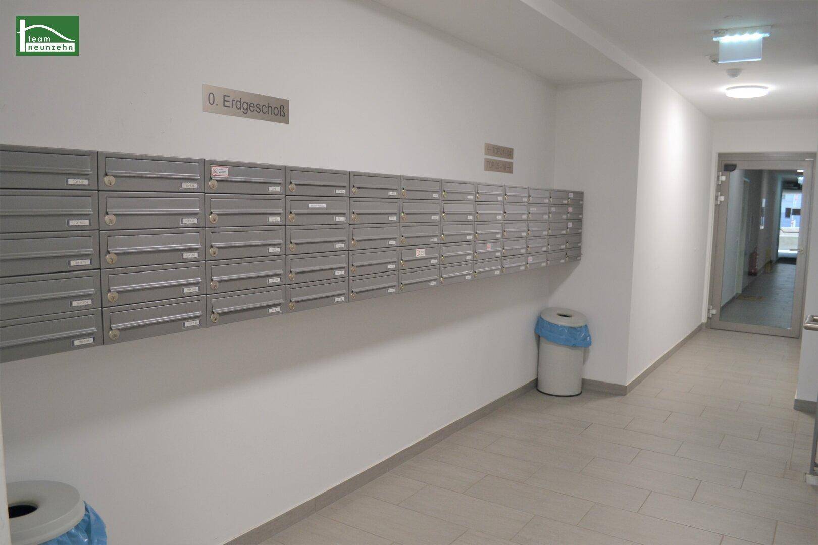 Langer, heller Flur im Erdgeschoss mit einer Wand voller Briefkästen und Fliesenboden.