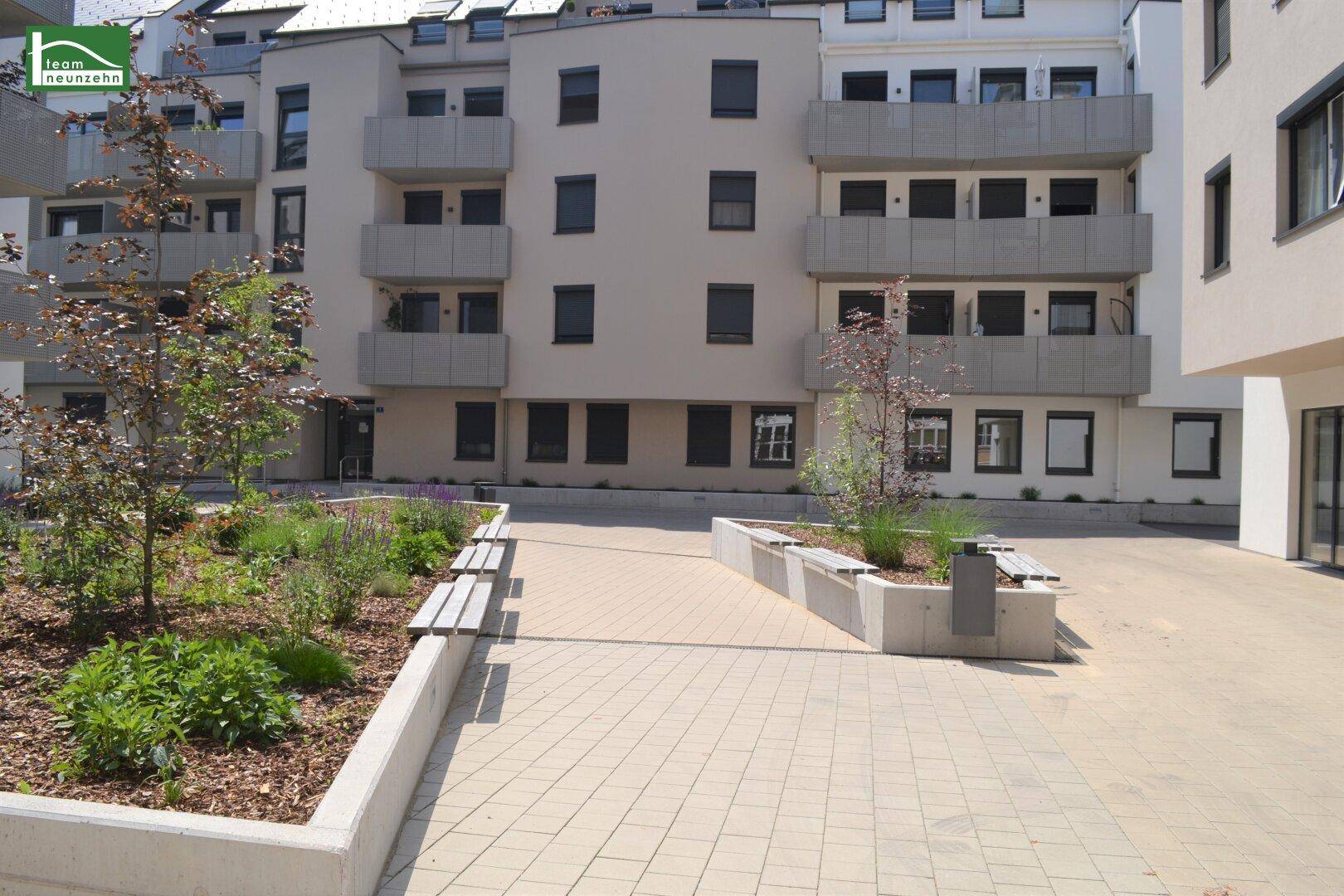 Moderner Innenhof mit gepflegten Grünflächen, Sitzbänken und neuen Wohngebäuden.