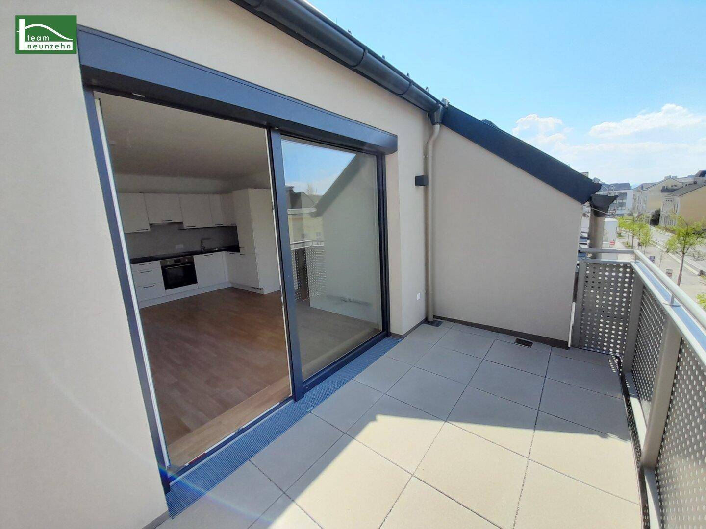 Geräumiger Balkon mit Fliesenboden und Blick in den offenen Wohn- und Küchenbereich.
