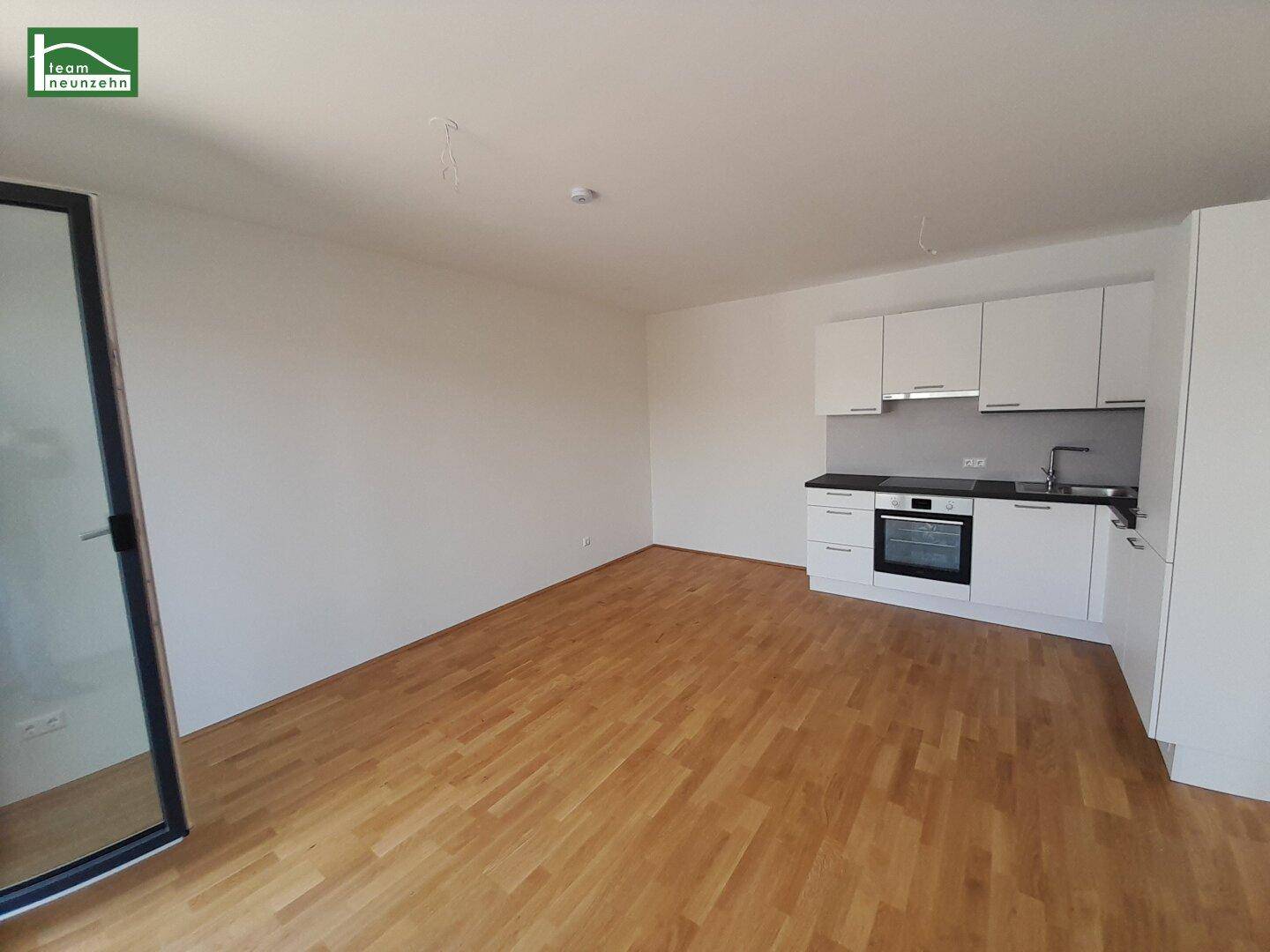 Offener Küchenbereich mit weißer Einbauküche, dunkler Arbeitsplatte und Holzboden.