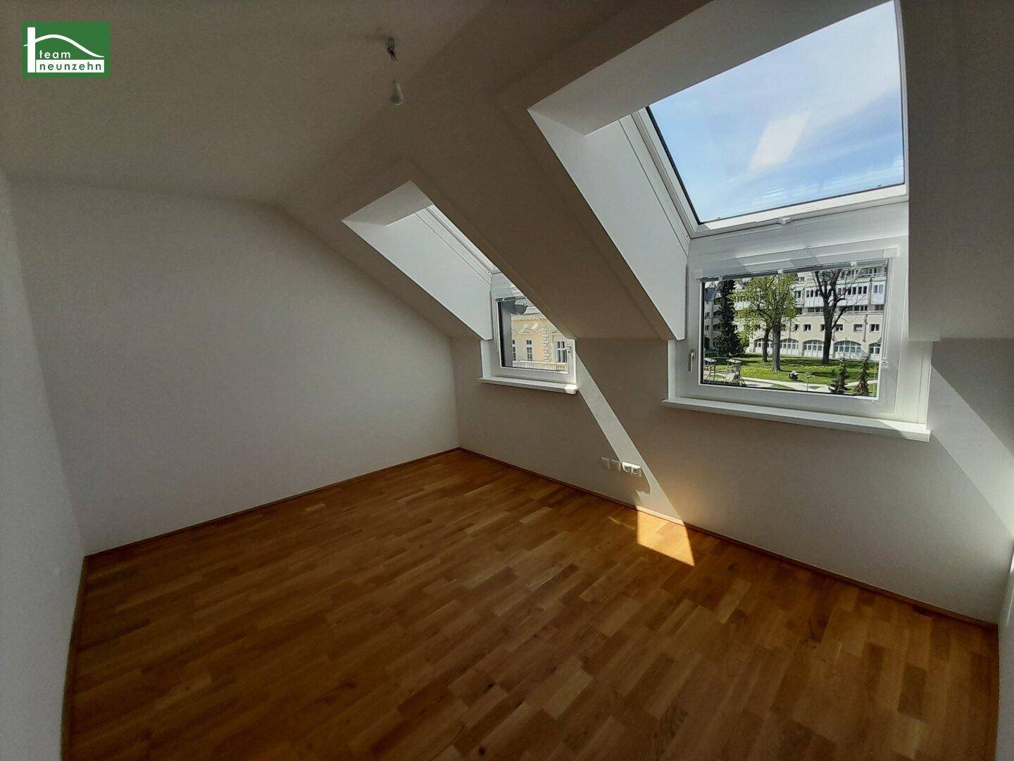 Helles Zimmer im Dachgeschoss mit Holzboden, Dachschrägen und mehreren Fenstern.