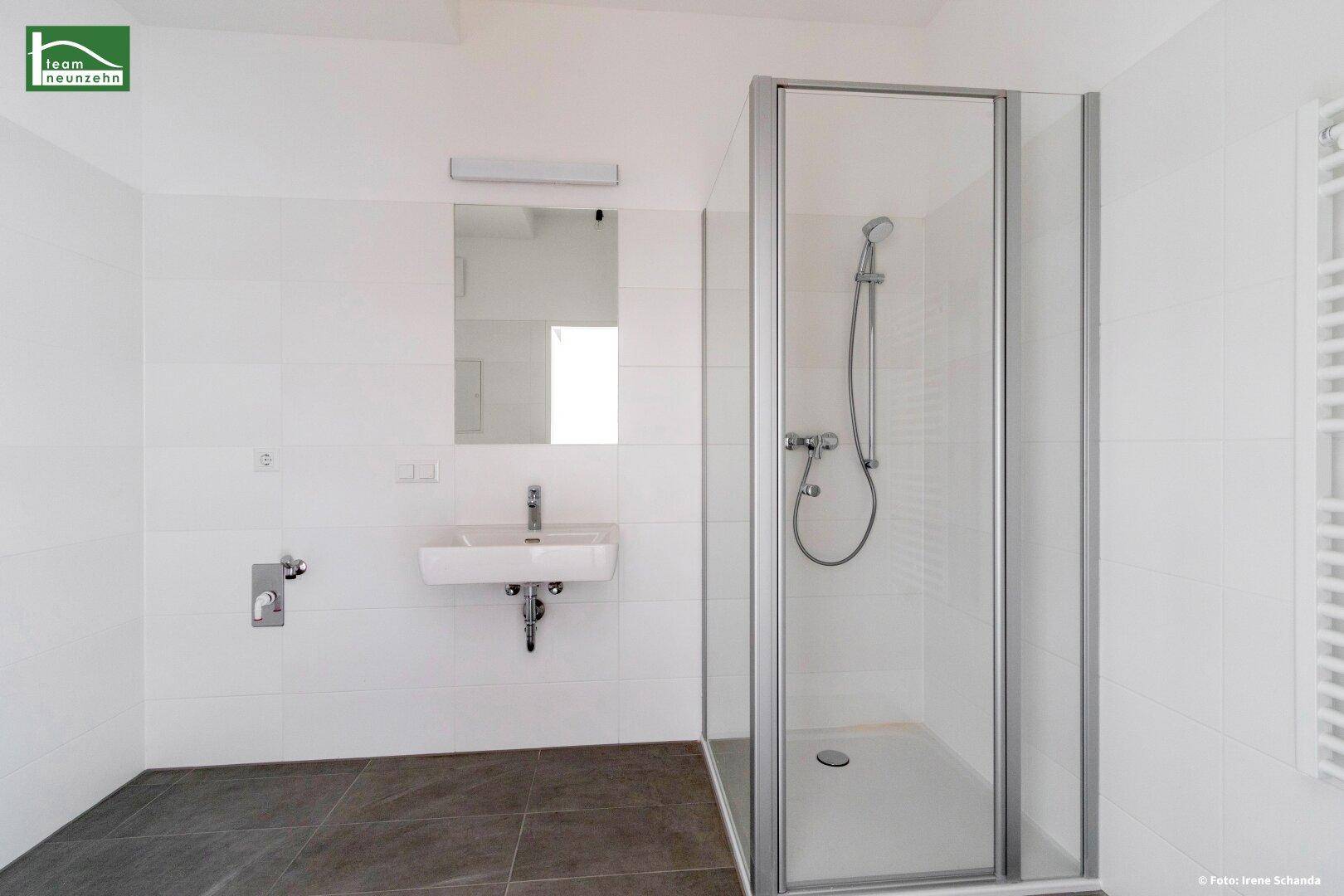 Modernes Badezimmer mit weißen Fliesen, Dusche und Waschbecken, in neuwertigem Zustand.