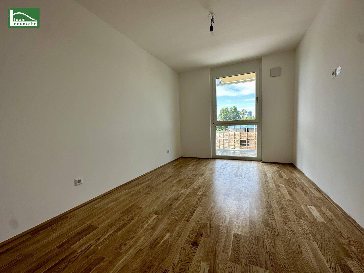 Helles Schlafzimmer mit Holzboden und großem Fenster, das viel Tageslicht hereinlässt.