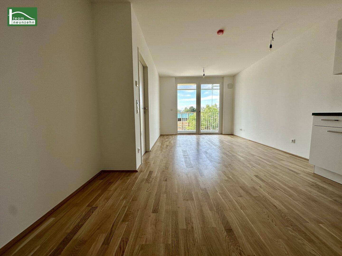 Geräumiger, heller Wohnbereich mit Holzboden und Zugang zu einem Balkon, bereit zur Einrichtung.