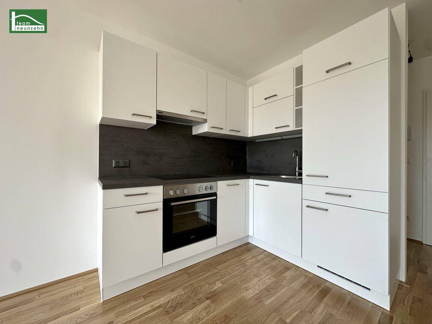 Moderne Einbauküche mit weißen Schränken, dunkler Arbeitsplatte und integrierten Geräten.