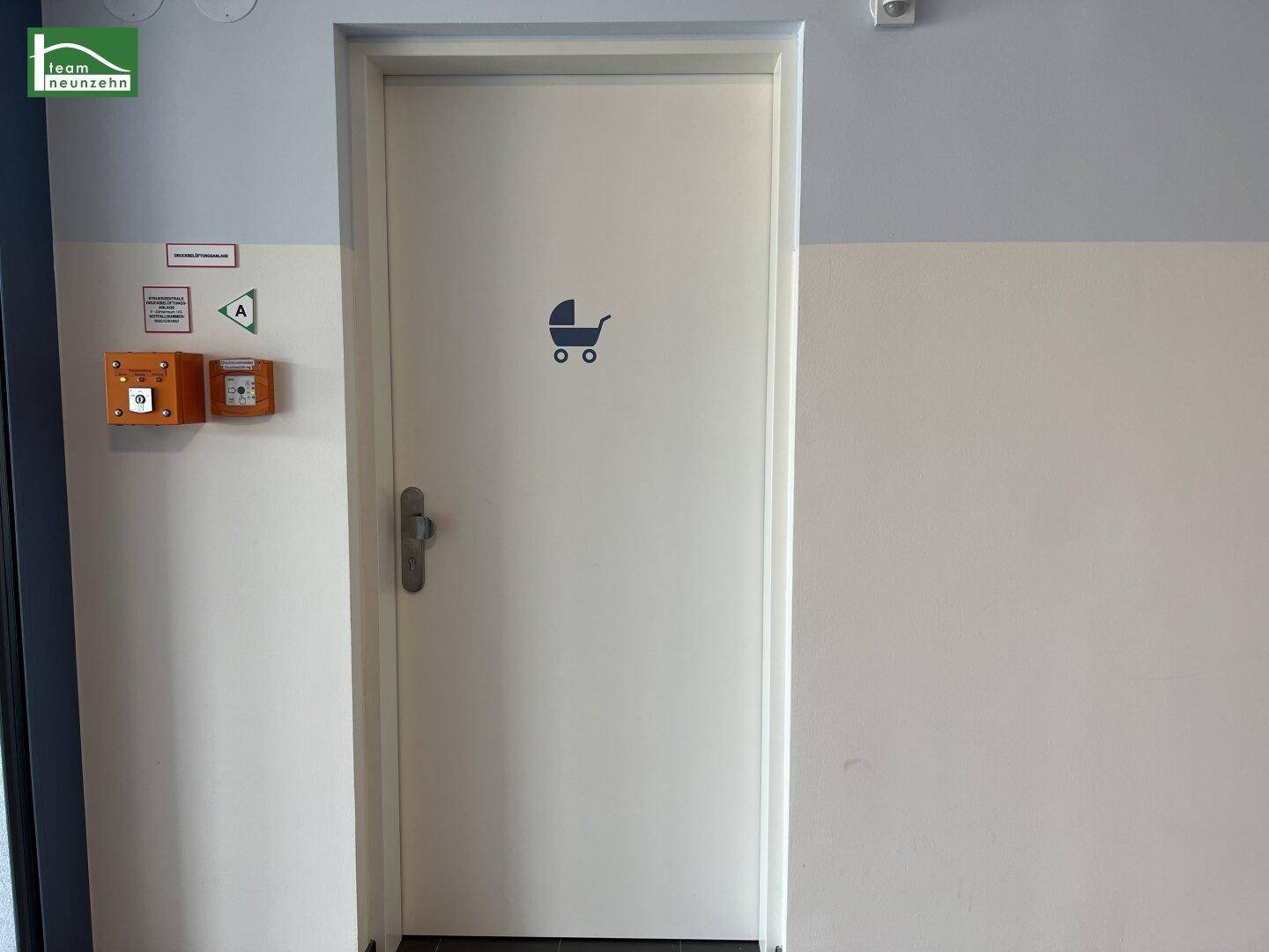 Tür zu einem Gemeinschaftsraum mit Kinderwagensymbol, wahrscheinlich ein Kinderwagenabstellraum.