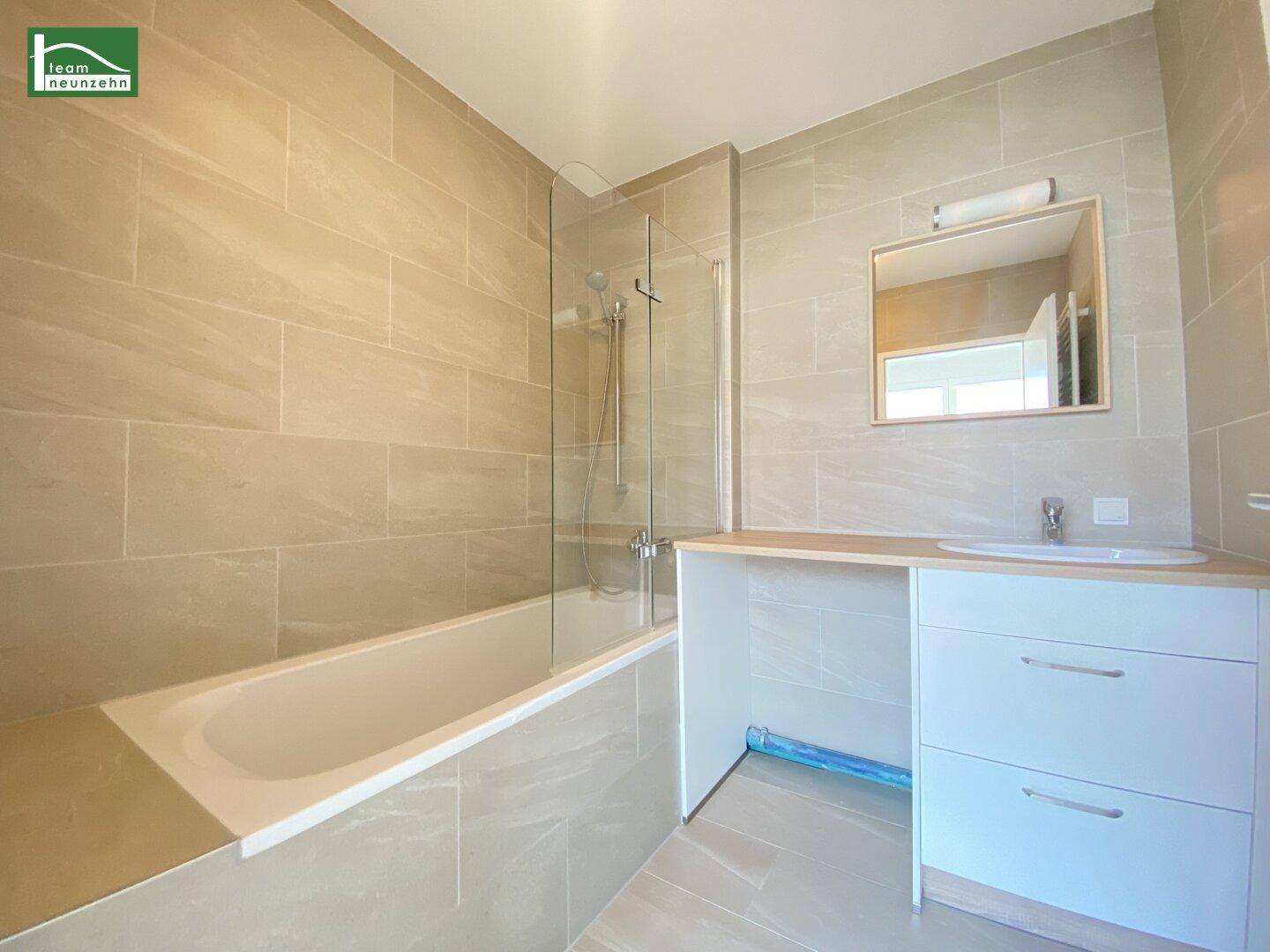 Modernes Badezimmer mit hellen Fliesen, Badewanne mit Duschwand und Einzelwaschbecken.