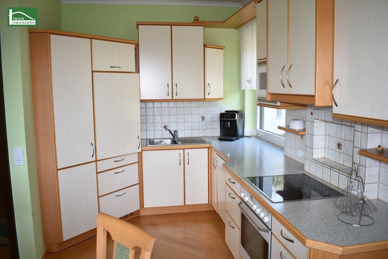 Funktionale Küche mit hellen Holzfronten, Einbaugeräten und grünen Wänden.