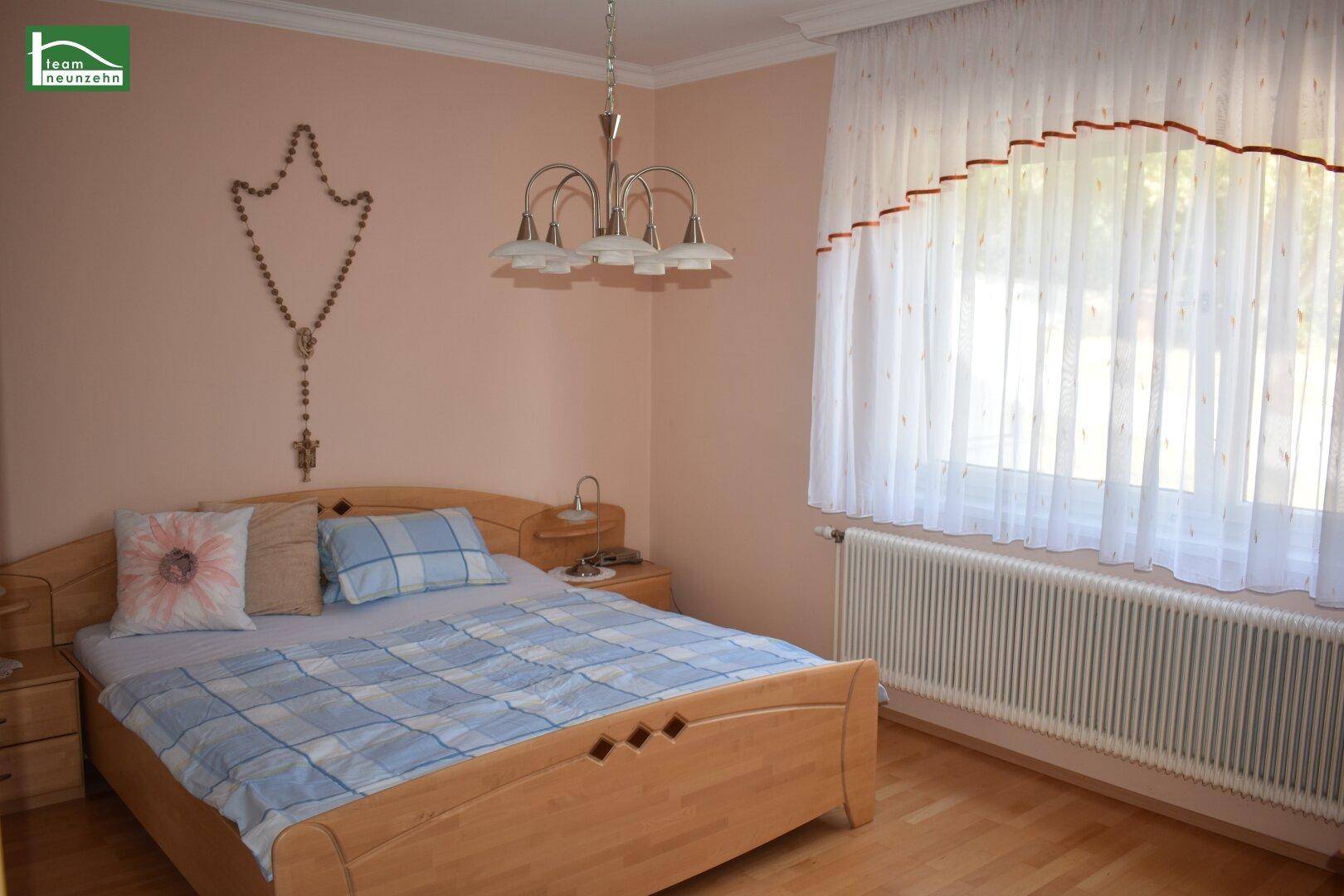 Helles Schlafzimmer mit Doppelbett, Holzmöbeln und Fenster mit Vorhängen.