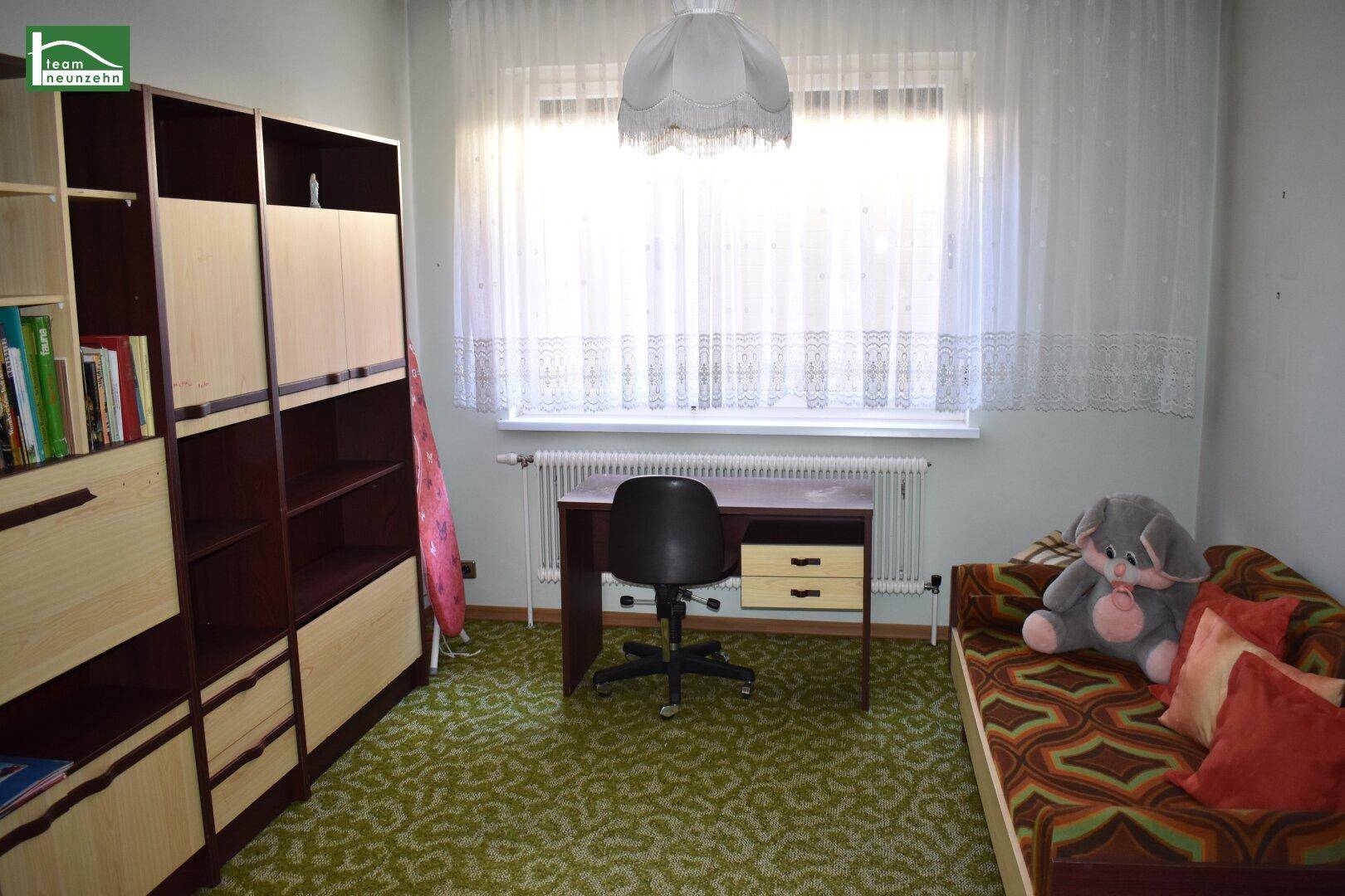 Kinderzimmer oder Gästezimmer mit Schreibtisch, Regal und Teppichboden.