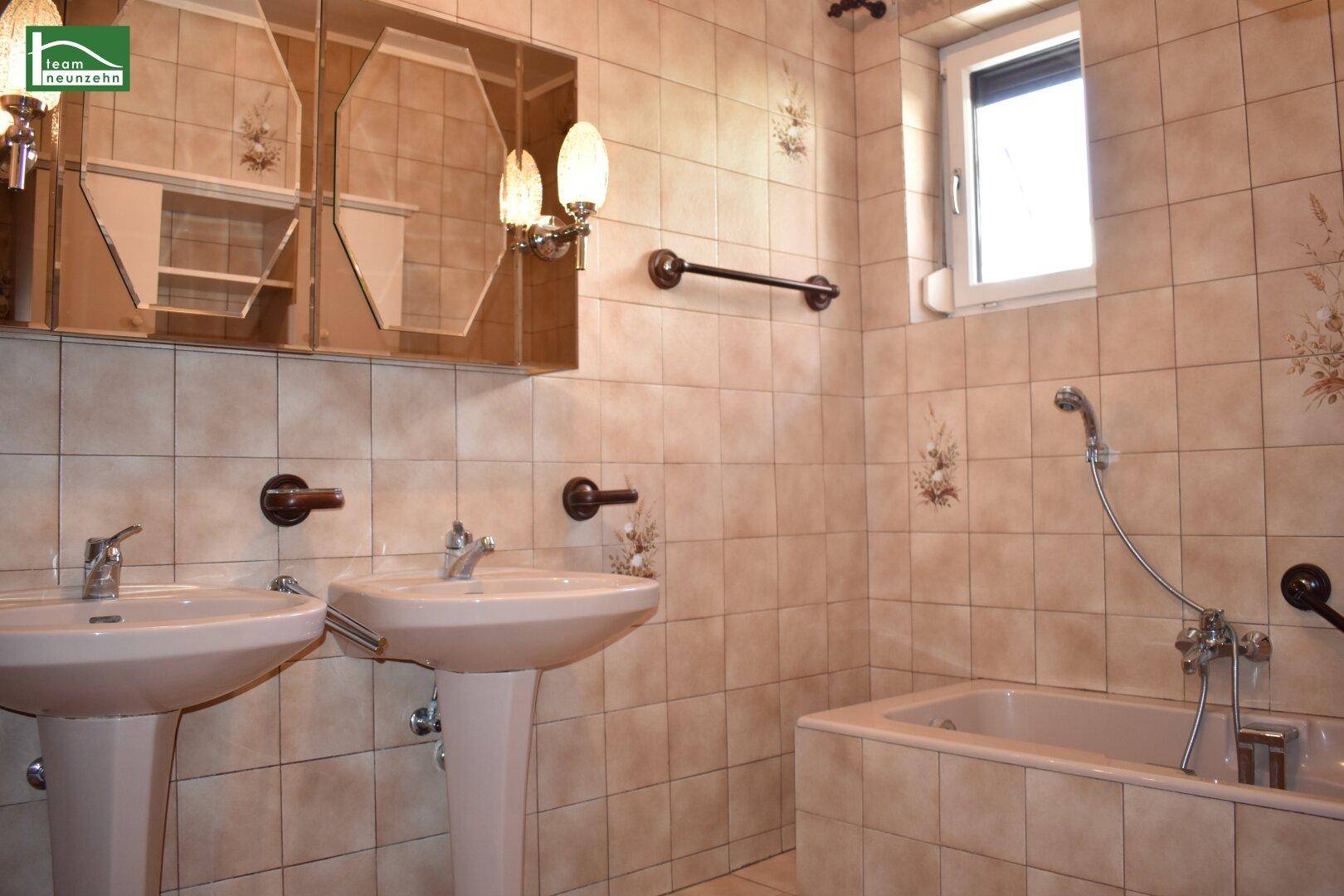 Badezimmer mit zwei Waschbecken, Badewanne und beigefarbenen Fliesen.
