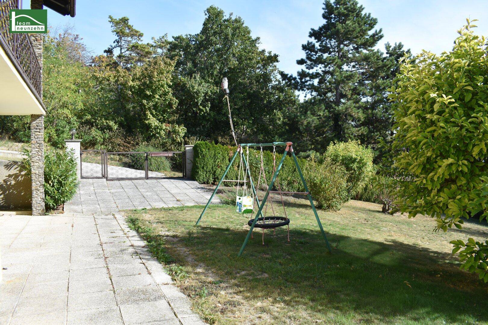 Gartenbereich mit Rasenfläche, Schaukel und gepflastertem Weg neben dem Haus.
