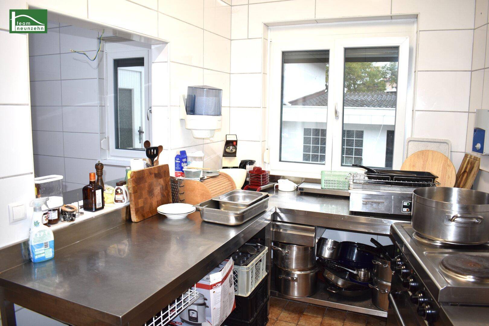 Helle Gewerbeküche mit Fenster, Edelstahlflächen und verschiedenen Kochutensilien.