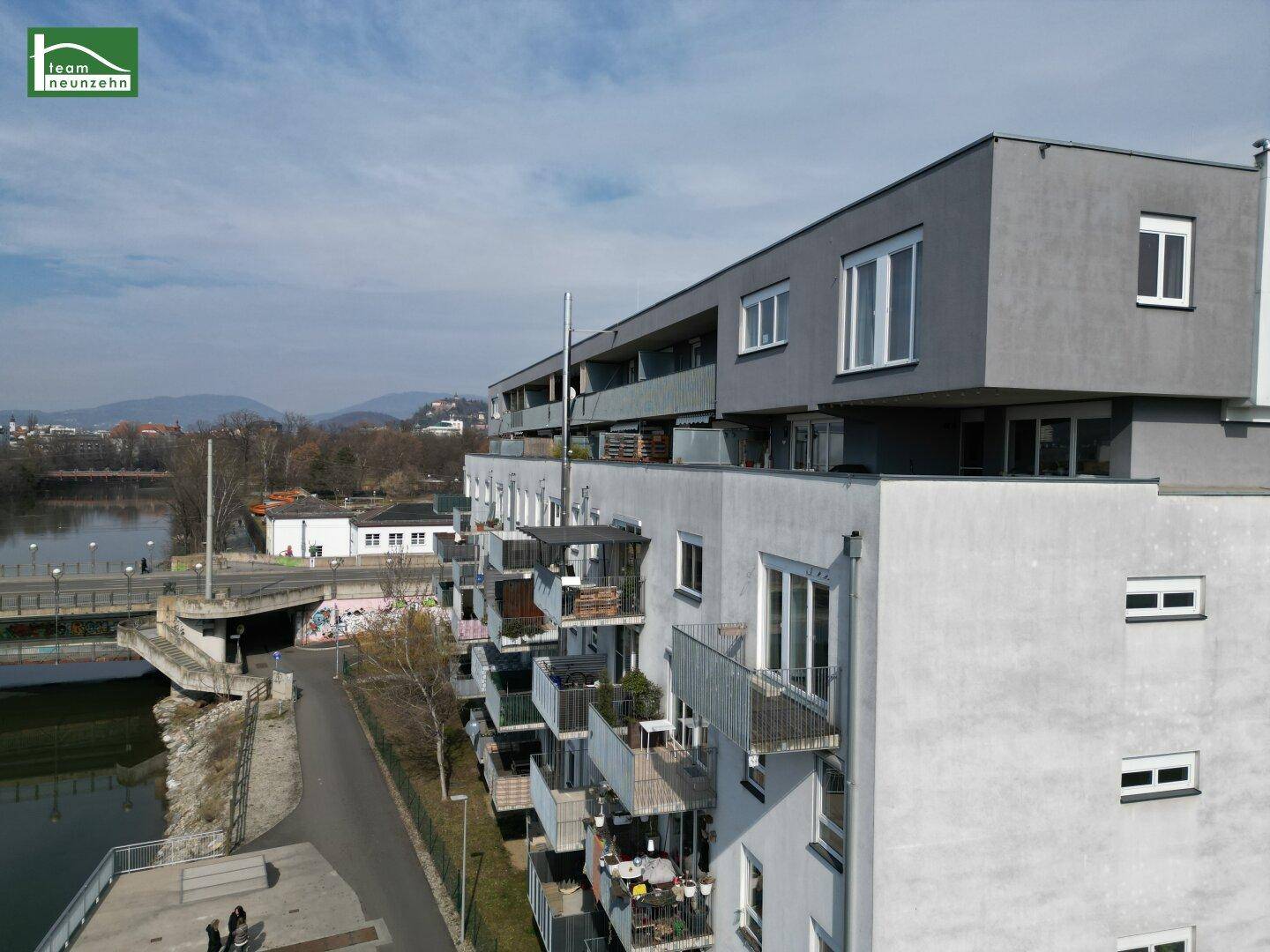 Wohngebäude am Fluss mit Balkonen und Ausblick auf die umliegende Stadtlandschaft.