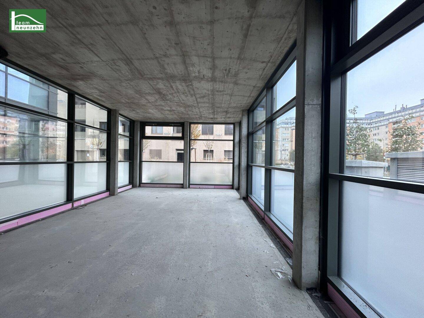 Unfertiger Gewerberaum mit großen Fenstern, Betonboden und -decke, bereit für den Ausbau.