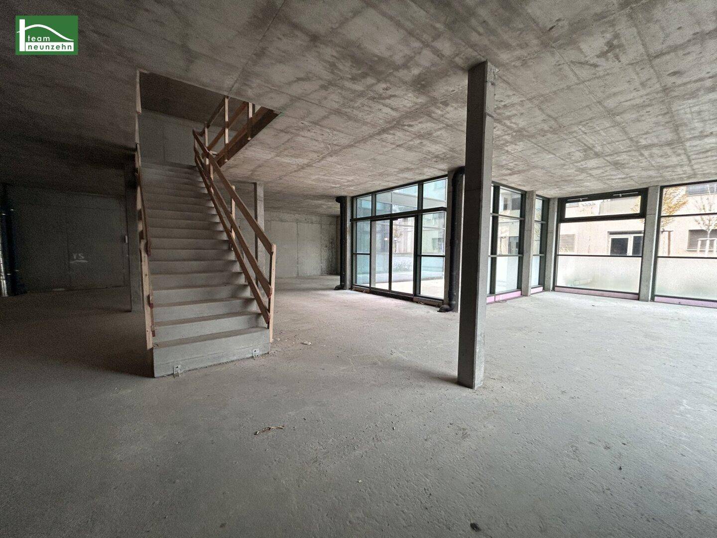 Großer, unfertiger Gewerberaum mit Betontreppe, hohen Decken und großen Fenstern.