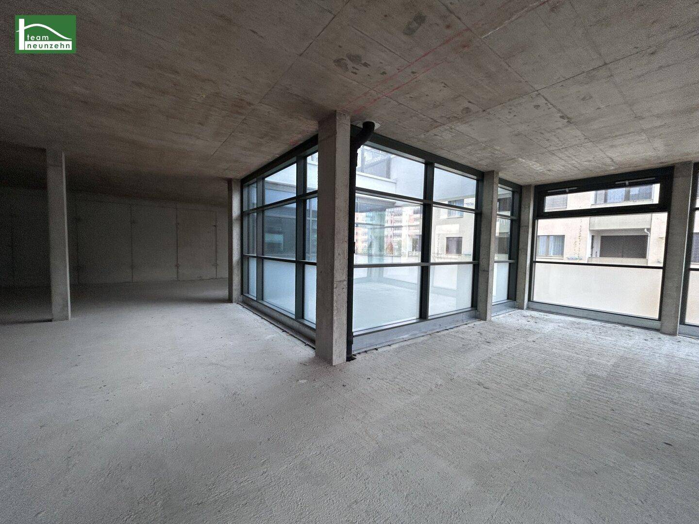 Eckbereich eines unfertigen Gewerberaums mit Betonoberflächen und großen Fenstern.